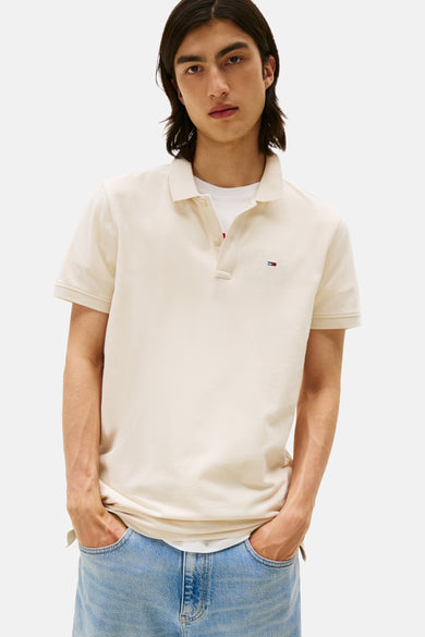 Polo beige à manches courtes de TOMMY JEANS, porté avec un t-shirt blanc et un jean délavé.
