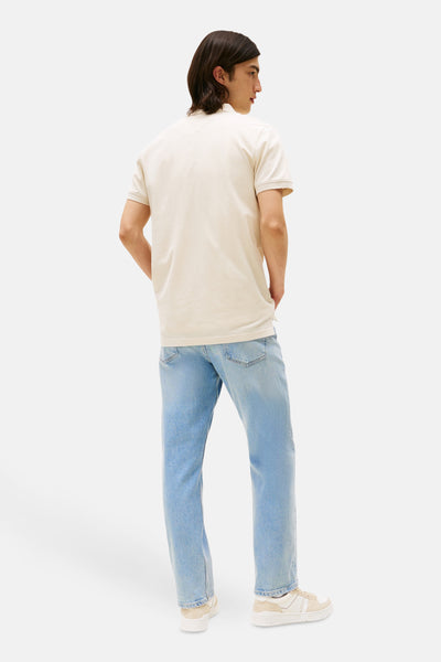 Polo à manches courtes beige de TOMMY JEANS, porté avec un jean bleu clair et des baskets blanches.