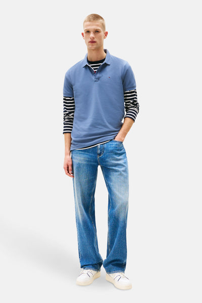 Polo bleu à manches courtes de TOMMY JEANS, porté avec un t-shirt rayé et un jean délavé