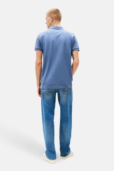 Polo bleu à manches courtes de TOMMY JEANS, porté avec un jean délavé et des baskets blanches, vue de dos.