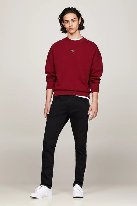 Jean fuselé noir de TOMMY JEANS, porté avec un pull rouge et des baskets blanches.