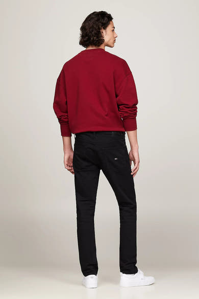 Jean fuselé noir de TOMMY JEANS, porté avec un pull rouge et des chaussures de sport blanches.