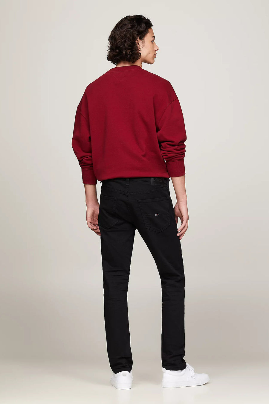 Jean fuselé noir de TOMMY JEANS, porté avec un pull rouge et des chaussures de sport blanches.