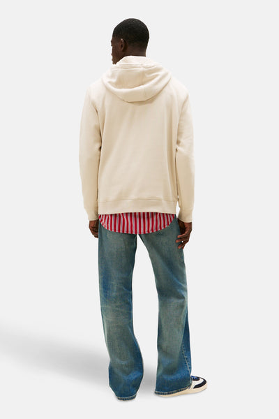 Sweat à capuche beige de TOMMY JEANS, porté avec une chemise rayée rouge et un jean délavé.