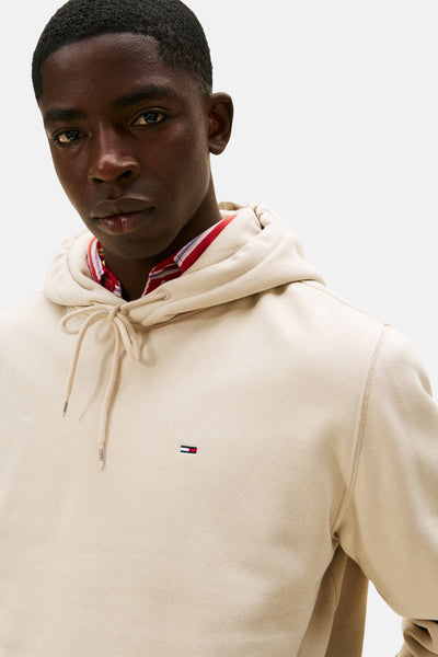Beige hoodie van Tommy Jeans, met trekkoord en klein vlaglogo op de voorkant, gedragen over een geruit overhemd.