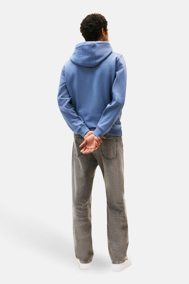 Sweat à capuche bleu de TOMMY JEANS, porté avec un jean gris délavé et des baskets blanches, vue de dos.