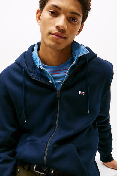 Gilet bleu de Tommy Jeans avec fermeture éclair et capuche, porté sur une chemise en jean claire