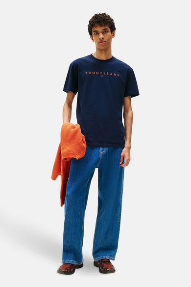 Blauw T-shirt met korte mouwen van TOMMY JEANS, gedragen met een oranje vest en een wijde blauwe jeans.