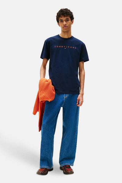 Blauw T-shirt met korte mouwen van TOMMY JEANS, gedragen met een oranje vest en een wijde blauwe jeans.