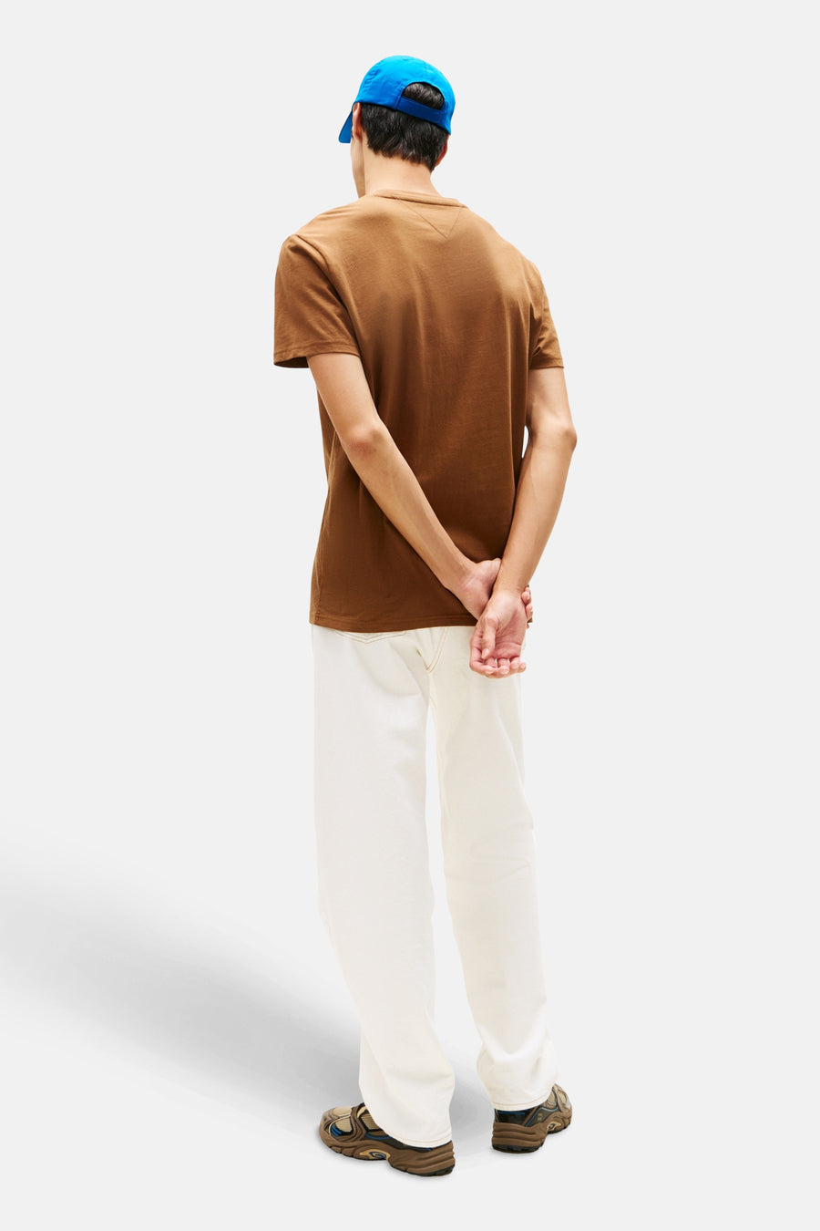 Bruin T-shirt met korte mouwen van Tommy Jeans, gedragen met gebroken witte broek en een blauwe pet.