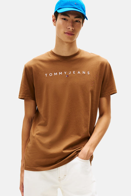 Bruin T-shirt met korte mouwen van TOMMY JEANS, gedragen met een witte broek en een blauwe pet.