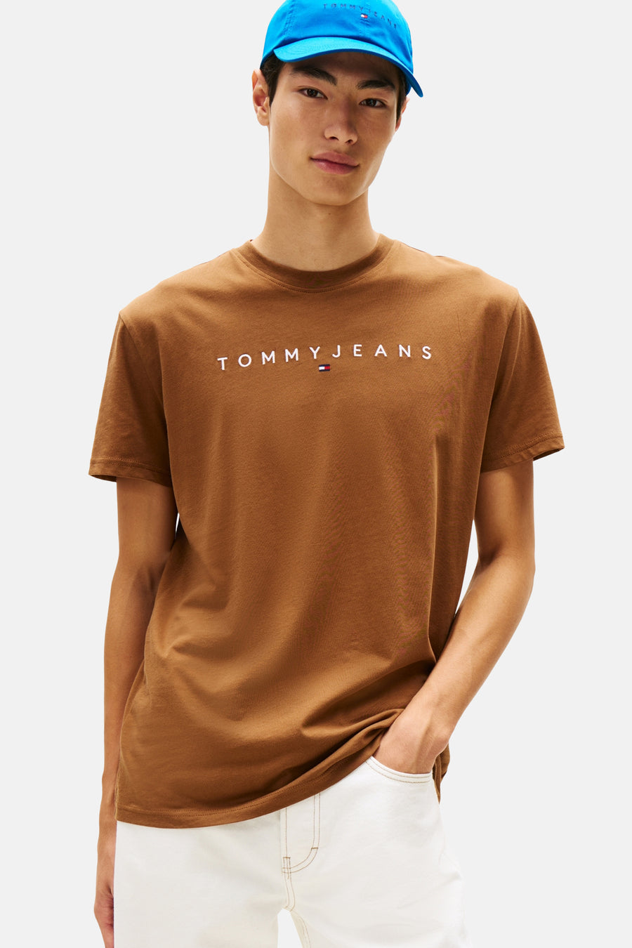 Bruin T-shirt met korte mouwen van TOMMY JEANS, gedragen met een witte broek en een blauwe pet.
