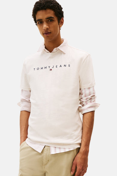 Beige T-shirt met korte mouwen van TOMMY JEANS, gedragen over een roze en wit gestreept overhemd, met een beige broek.
