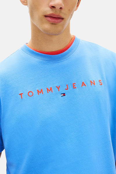 Bright blue short-sleeve t-shirt with red ribbed collar and orange embroidered TOMMYJEANS logo by Tommy Jeans, shown in close-up front view.
