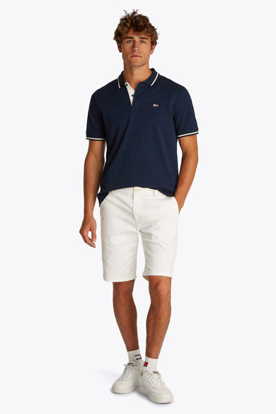 Donkerblauwe polo met korte mouwen van TOMMY JEANS met contrasterende kraag, gedragen met een witte korte broek en witte sneakers.