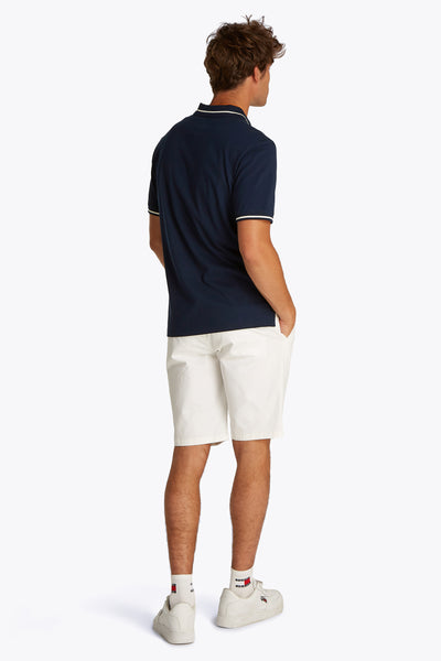 Blauw poloshirt met korte mouwen van TOMMY JEANS, gedragen met een witte korte broek en witte sneakers.