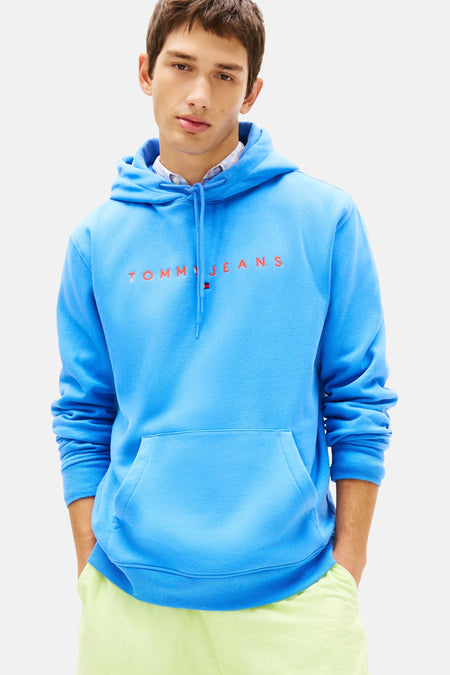 Blauwe hoodie van Tommy Jeans, gedragen met een gele korte broek en bruine bootschoenen.