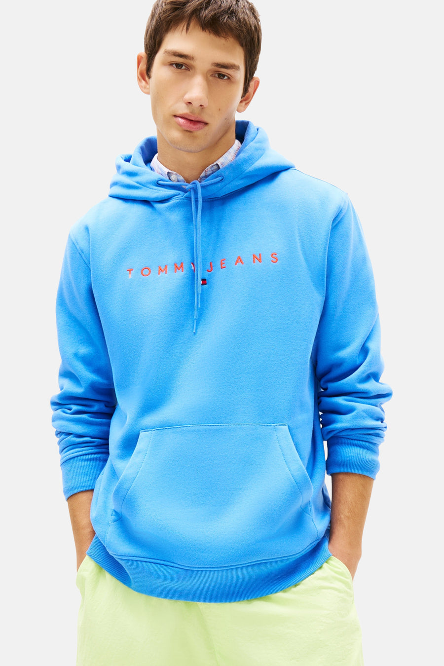 Blauwe hoodie van Tommy Jeans, gedragen met een gele korte broek en bruine bootschoenen.
