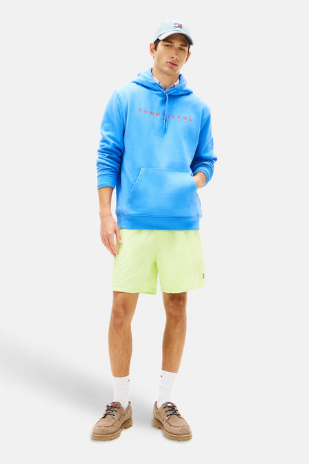 Sweat à capuche bleu de Tommy Jeans, porté avec un short jaune et des chaussures bateau marron.