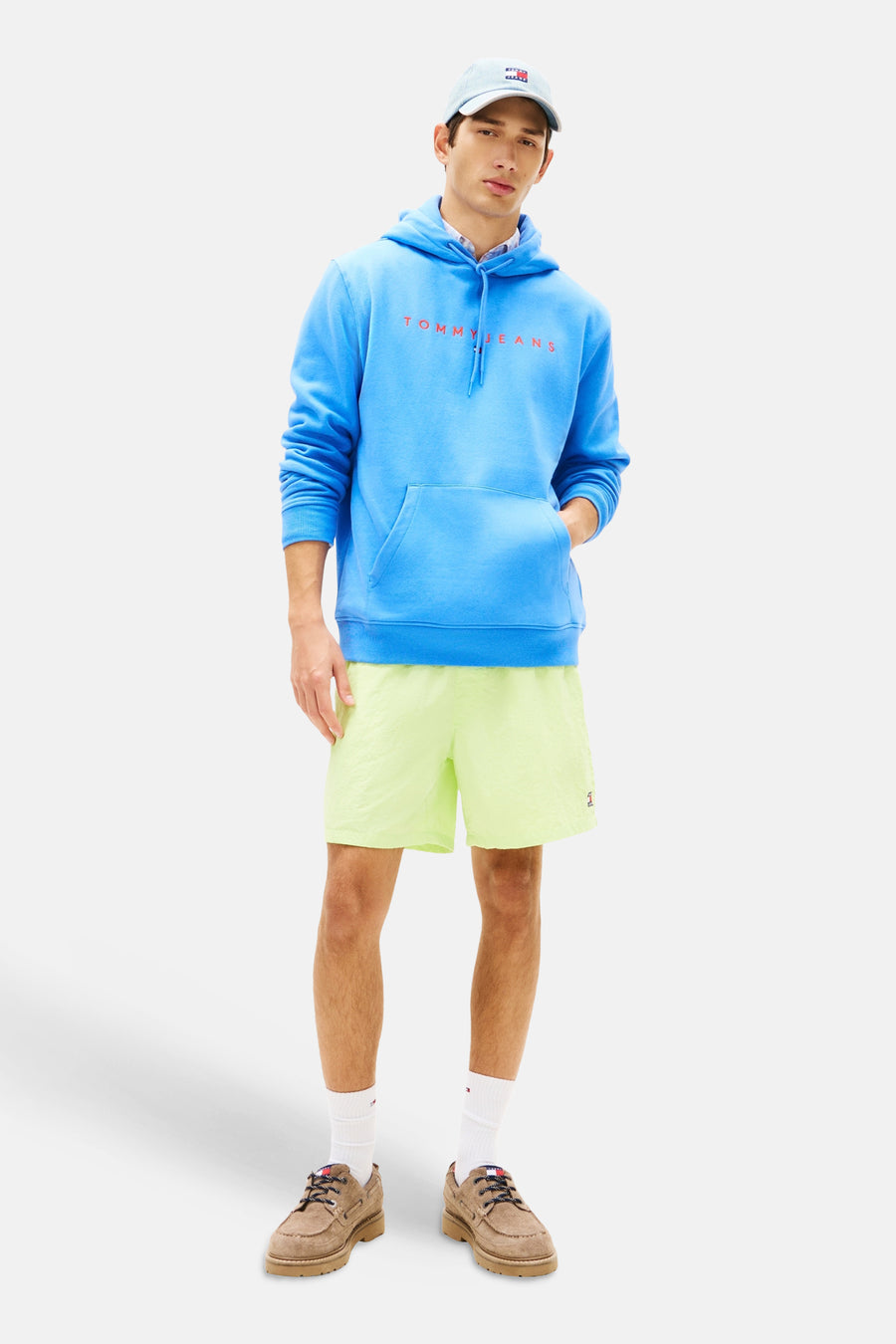 Sweat à capuche bleu de Tommy Jeans, porté avec un short jaune et des chaussures bateau marron.