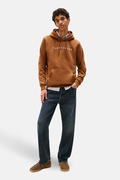 Bruine hoodie van TOMMY JEANS, met trekkoord en kangoeroezak, gedragen over een overhemd en een casual spijkerbroek.