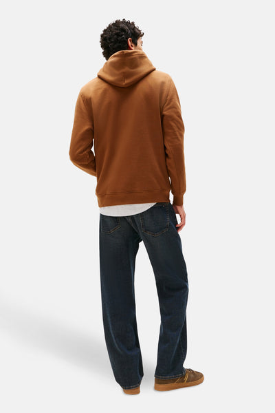 Bruine hoodie van TOMMY JEANS, gedragen met een gestreept overhemd en een wijde blauwe jeans.