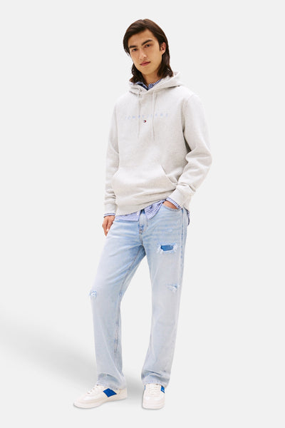 Grijze hoodie van TOMMY JEANS met een effen patroon, gedragen over een geruit overhemd en een gescheurde spijkerbroek.