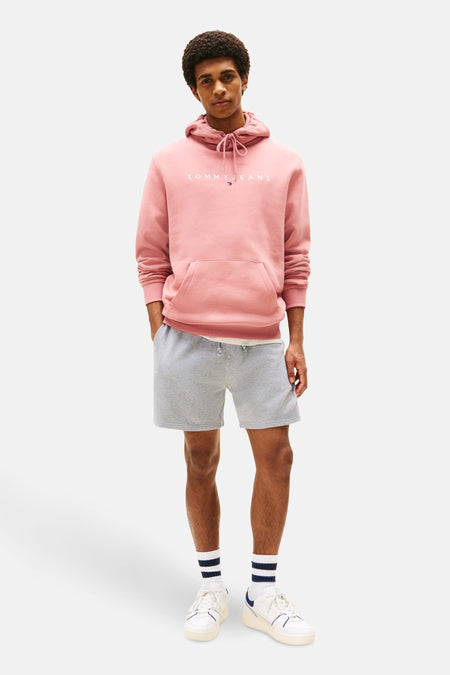 Roze hoodie van TOMMY JEANS, gedragen met een gemêleerde grijze short, gestreepte sokken en witte sneakers.