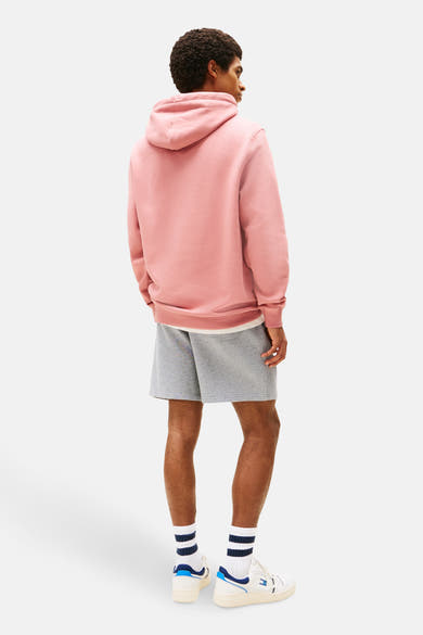 Sweat à capuche rose de Tommy Jeans, porté avec un short gris et des baskets blanches.