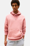 Sweat à capuche rose de TOMMY JEANS, avec cordon de serrage et poche kangourou, porté avec un pantalon de survêtement gris.
