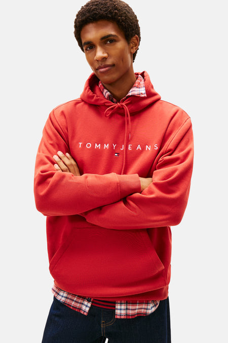 Rode hoodie van TOMMY JEANS gedragen met een geruit overhemd en een wijde jeans.