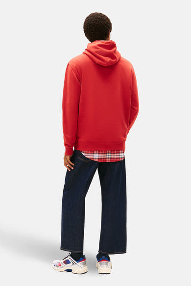 Rode hoodie van TOMMY JEANS, gedragen met een geruit overhemd en een wijde jeans, van achteren gezien.