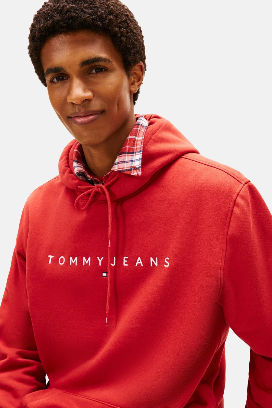 Rode TOMMY JEANS hoodie met trekkoord, gedragen over een geruit overhemd.