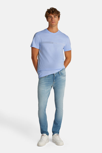 Blauw T-shirt met korte mouwen van TOMMY JEANS, met decoratieve strepen, gedragen met een spijkerbroek en witte sneakers.