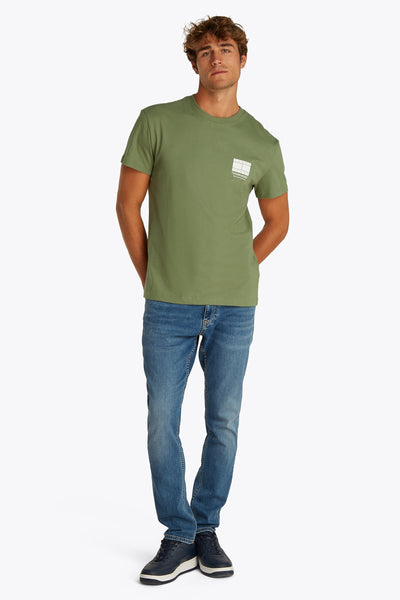 Groen T-shirt met korte mouwen van TOMMY JEANS, met een wit logo op de borst, gedragen met een blauwe jeans en marineblauwe sneakers.