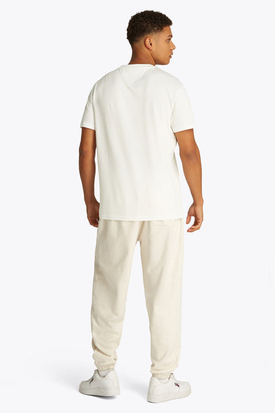 Wit T-shirt met korte mouwen van TOMMY JEANS, met een discreet logo op de rug, gedragen met een joggingbroek en sneakers.
