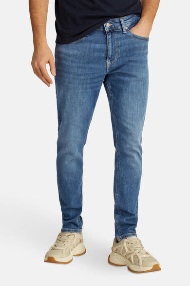 Tommy Jeans lichtblauwe tapered jeans, gedragen met beige sneakers.