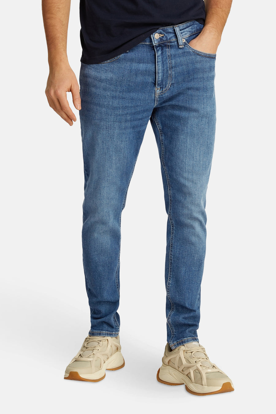 Tommy Jeans lichtblauwe tapered jeans, gedragen met beige sneakers.