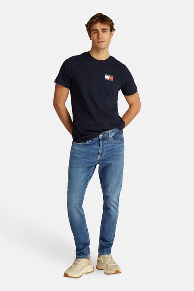 Lichtblauwe tapered jeans van TOMMY JEANS, gedragen met een marineblauw T-shirt en beige sneakers.