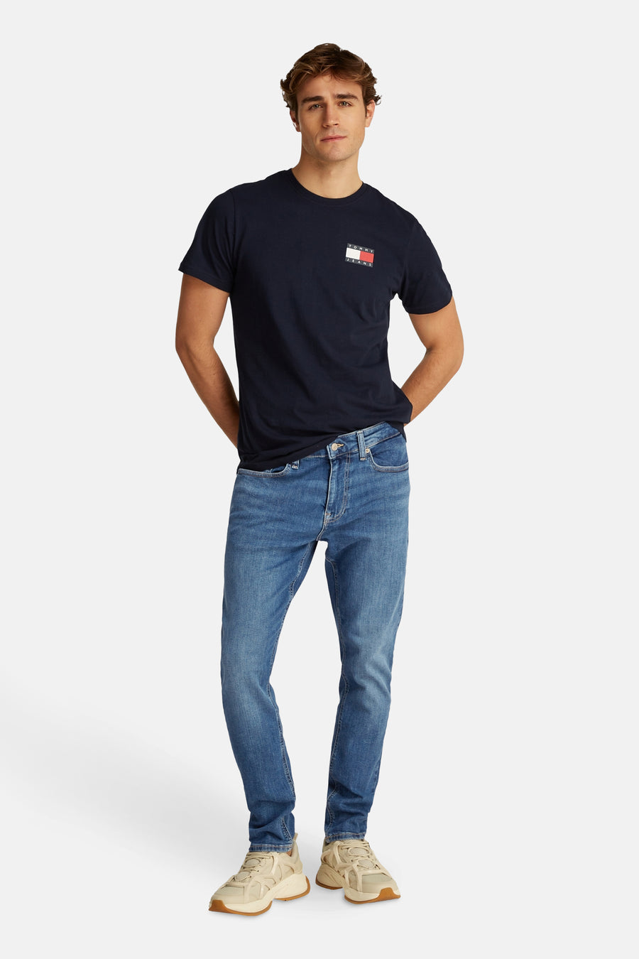 Lichtblauwe tapered jeans van TOMMY JEANS, gedragen met een marineblauw T-shirt en beige sneakers.