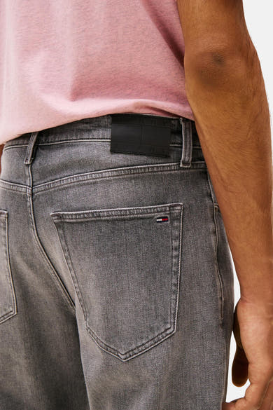 Grijze tapered jeans van Tommy Jeans, met zwart leren etiket en driekleurige stiksels op de zak.
