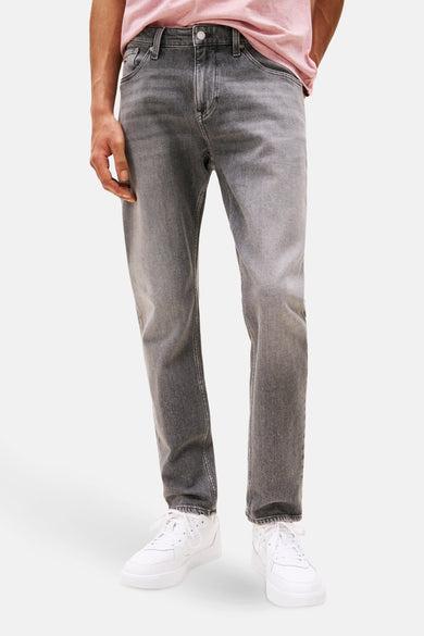 Jean tapered gris délavé de TOMMY JEANS, porté avec des baskets blanches et un t-shirt rose.