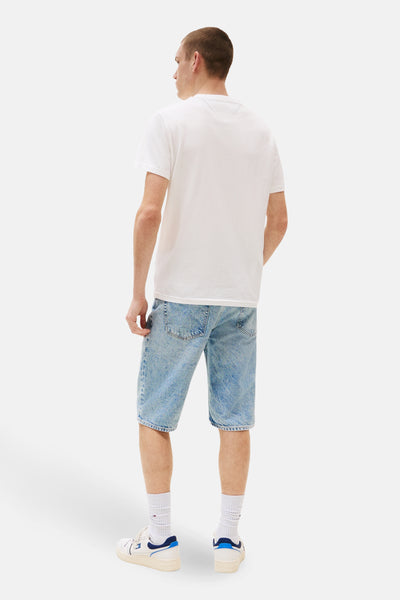 T-shirt à manches courtes blanc de TOMMY JEANS, porté avec un short en jean et des baskets blanches.
