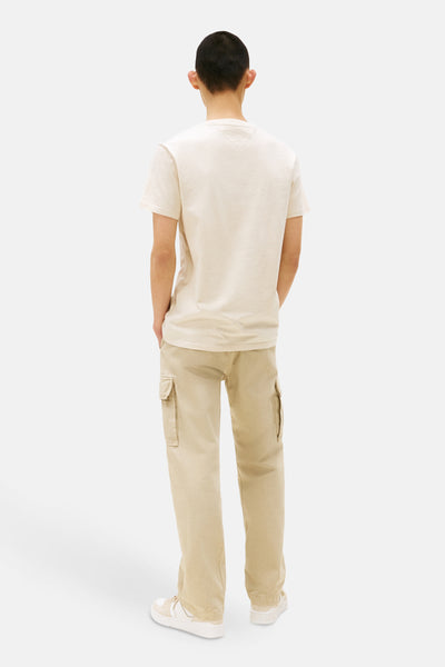 T-shirt à manches courtes écru de TOMMY JEANS, uni, porté avec un pantalon cargo beige et des baskets blanches.