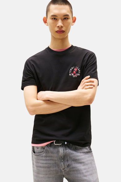 T-shirt noir à manches courtes de TOMMY JEANS avec un logo imprimé sur la poitrine, porté avec un jean gris.
