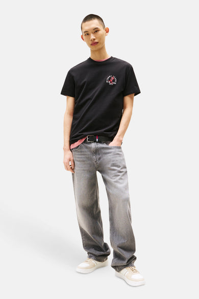 T-shirt noir à manches courtes de TOMMY JEANS, avec un logo imprimé, porté avec un jean gris délavé et des baskets.
