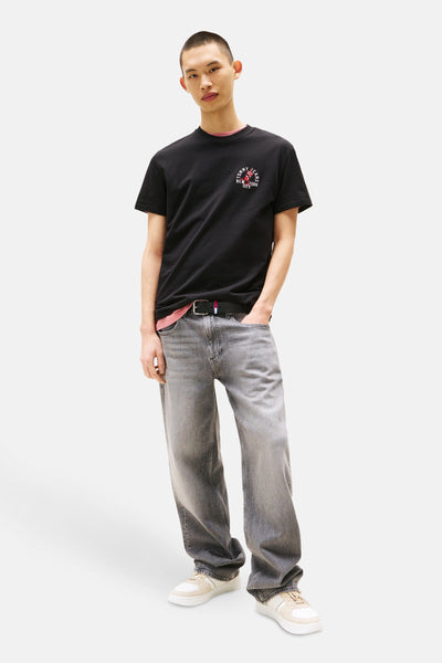 T-shirt noir à manches courtes de TOMMY JEANS, avec un logo imprimé, porté avec un jean gris délavé et des baskets.