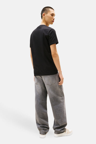 T-shirt à manches courtes noir de TOMMY JEANS, avec un jean gris délavé et des baskets couleur crème.