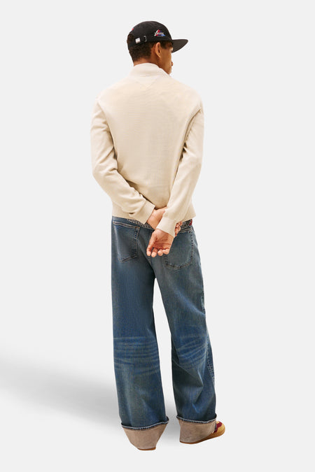 Sweat-shirt beige à col montant de Tommy Jeans, porté avec un pantalon ample et une casquette noire.
