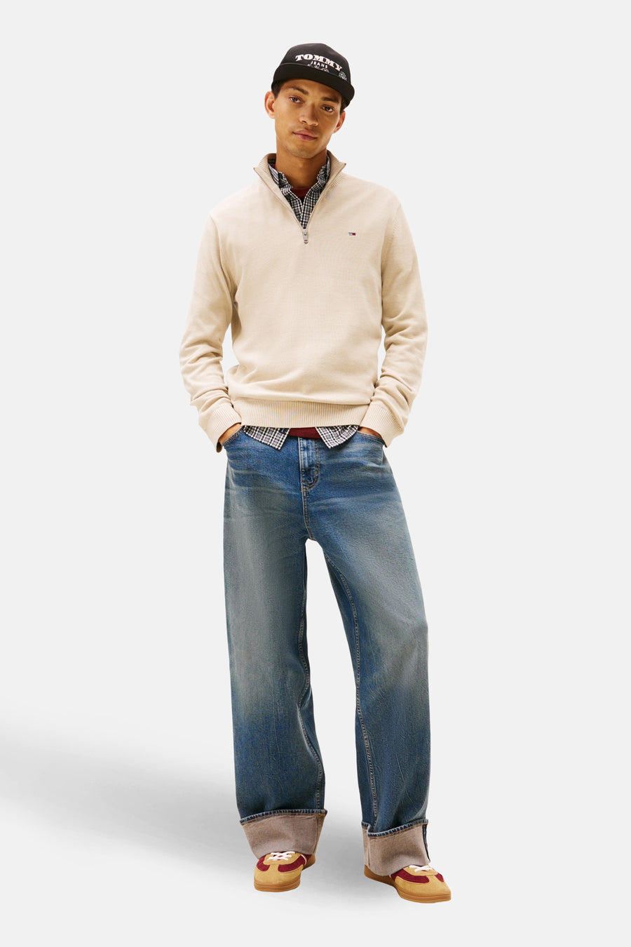 Beige sweat-shirt à col montant van TOMMY JEANS, gedragen over een geruit overhemd, met een wijde jeans en sportschoenen.